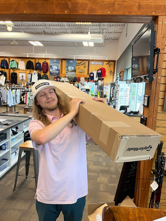 Retail inventory associate processing a TaylorMade shipment in a professional golf and sports equipment showroom.