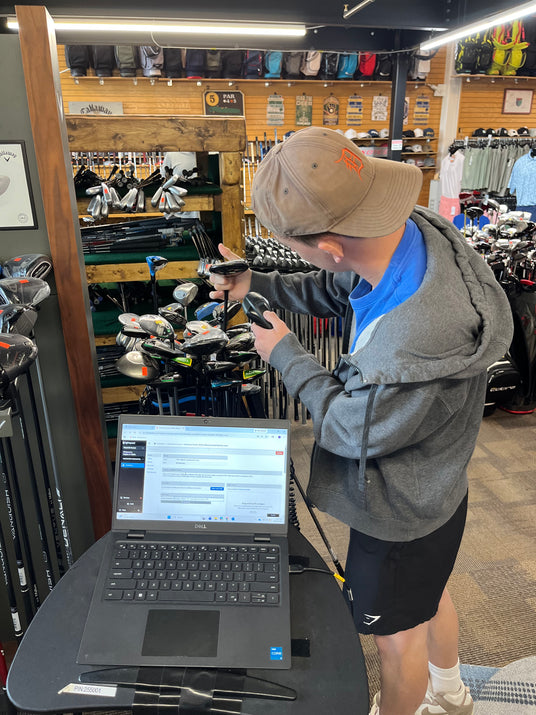 Retail inventory manager performing a stock audit on golf equipment using a mobile workstation and backend software.