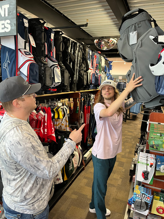 Retail associate managing golf equipment inventory and customer inquiries in a professional sports equipment showroom.