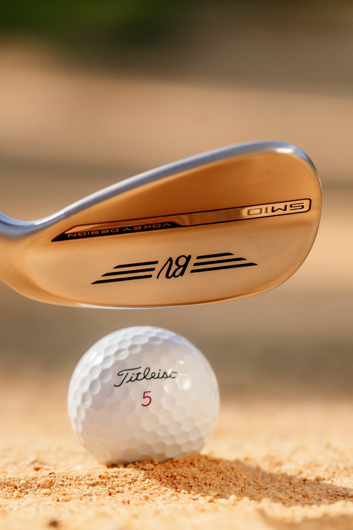 Wedge striking from sand highlighting its milled face, controlled launch, and spin‑focused design for bunker performance.