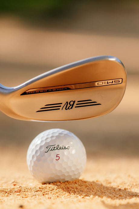 Wedge striking from sand highlighting its milled face, controlled launch, and spin‑focused design for bunker performance.
