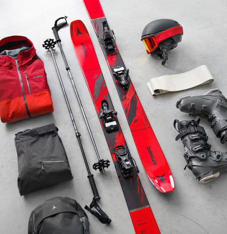 Premium alpine skiing equipment flat lay with downhill skis, technical outerwear, and backcountry touring gear for adults.