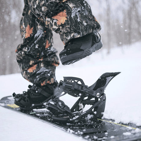 A rider securing their snowboard boots into high-performance bindings on a snowy slope, ready for mountain riding.