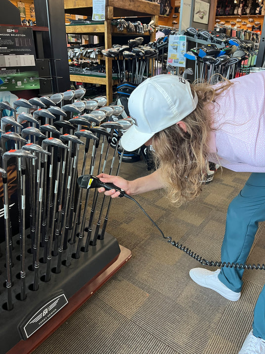 Retail inventory associate using a handheld scanner to manage golf equipment SKUs and showroom product availability.