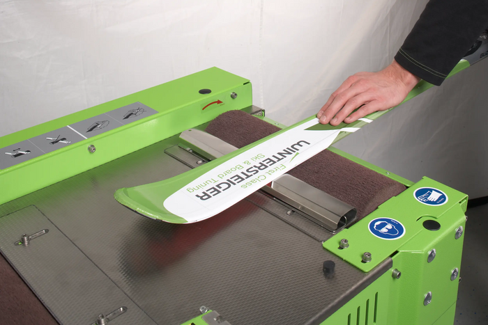 Professional Wintersteiger ski and snowboard machine waxing at our Oshkosh shop, ensuring a high-quality, even finish.