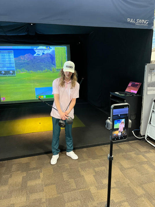 Marketing intern capturing video of indoor golf simulator services for promotional use in a sports retail environment.