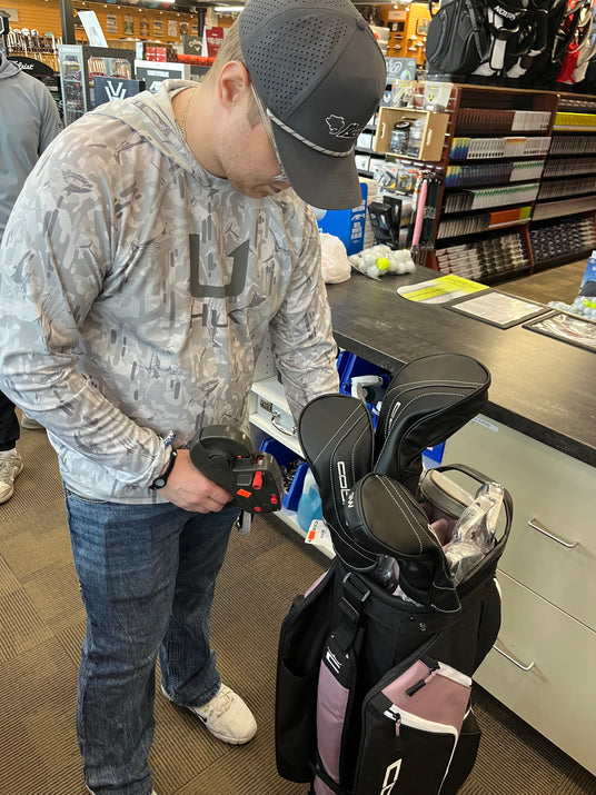 Retail merchandiser processing golf bag inventory and pricing at a pro shop counter for efficient showroom management.