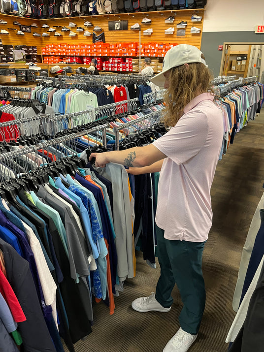Retail associate managing seasonal apparel inventory and floor merchandising in an upscale sports equipment showroom.